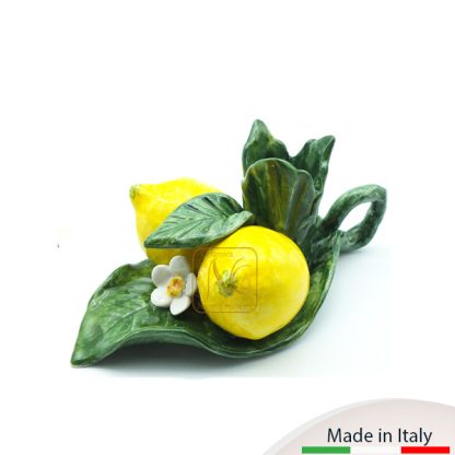 Bugia con due limoni adagiata su foglie con fiorellino e manico.